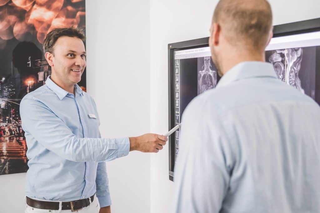 Dr. Demant erklärt Patienten etwas am Fernseher