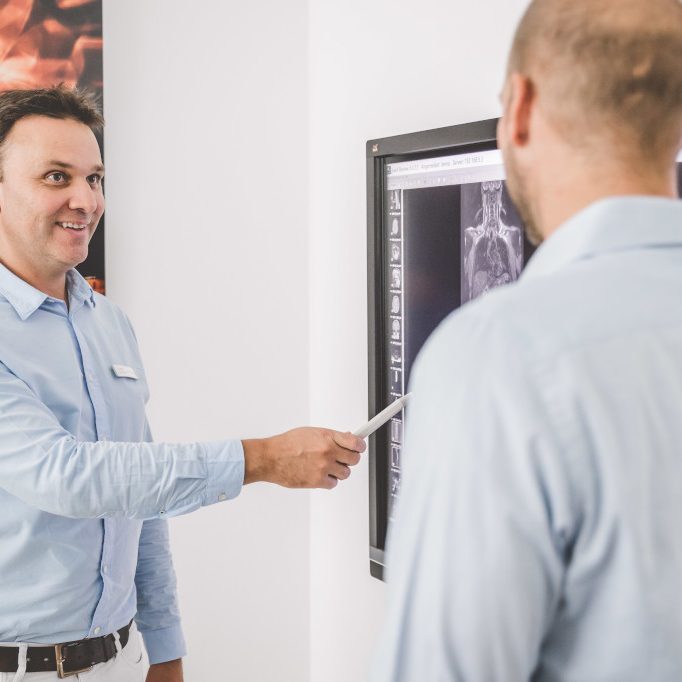 Dr. Demant erklärt Patienten etwas am Fernseher