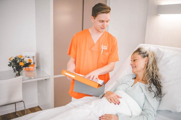 Pflegekraft der Beta Klinik informiert Patientin in ihrem Patientenzimmer