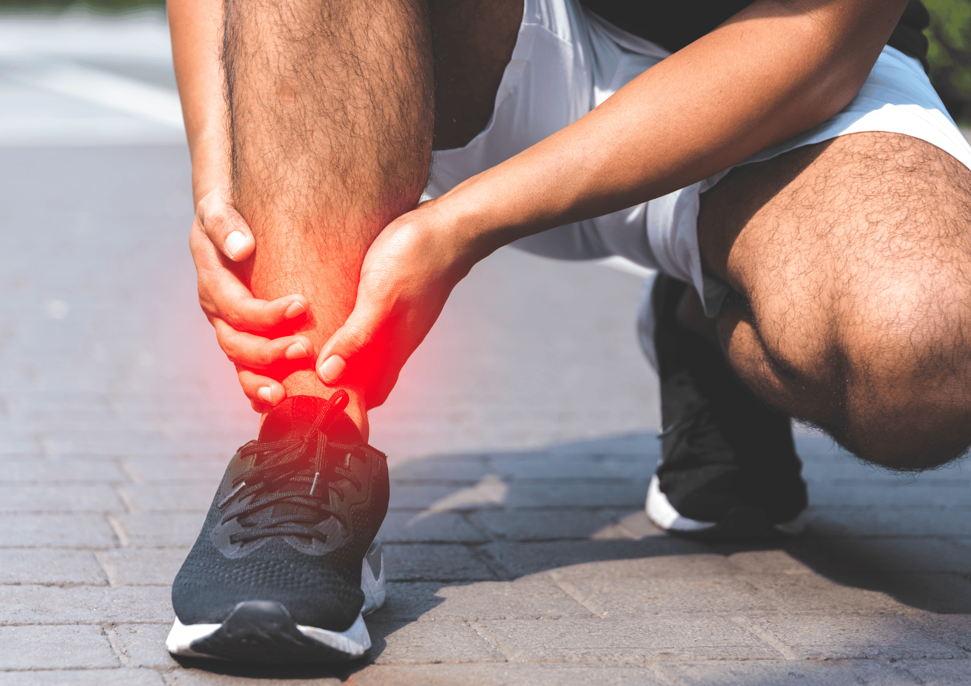 Person kniet auf Pflaster und hält schmerzenden Knöchel mit roten Sportschuhen.