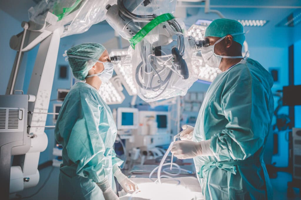 Zwei Chirurgen in OP-Kleidung operieren mit einem Mikroskop im Operationssaal.