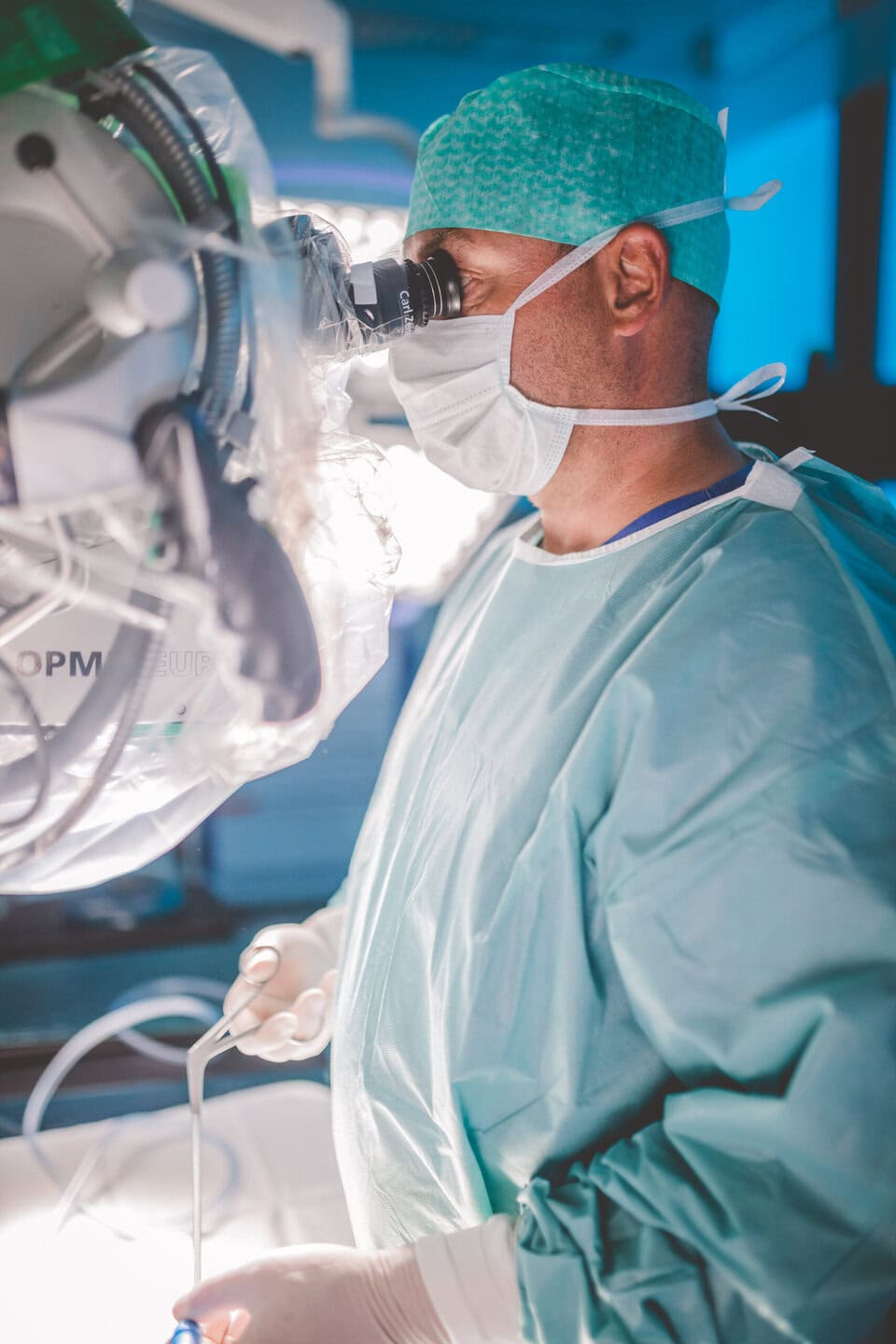 Ein Chirurg in OP-Kleidung arbeitet konzentriert mit einem Mikroskop.