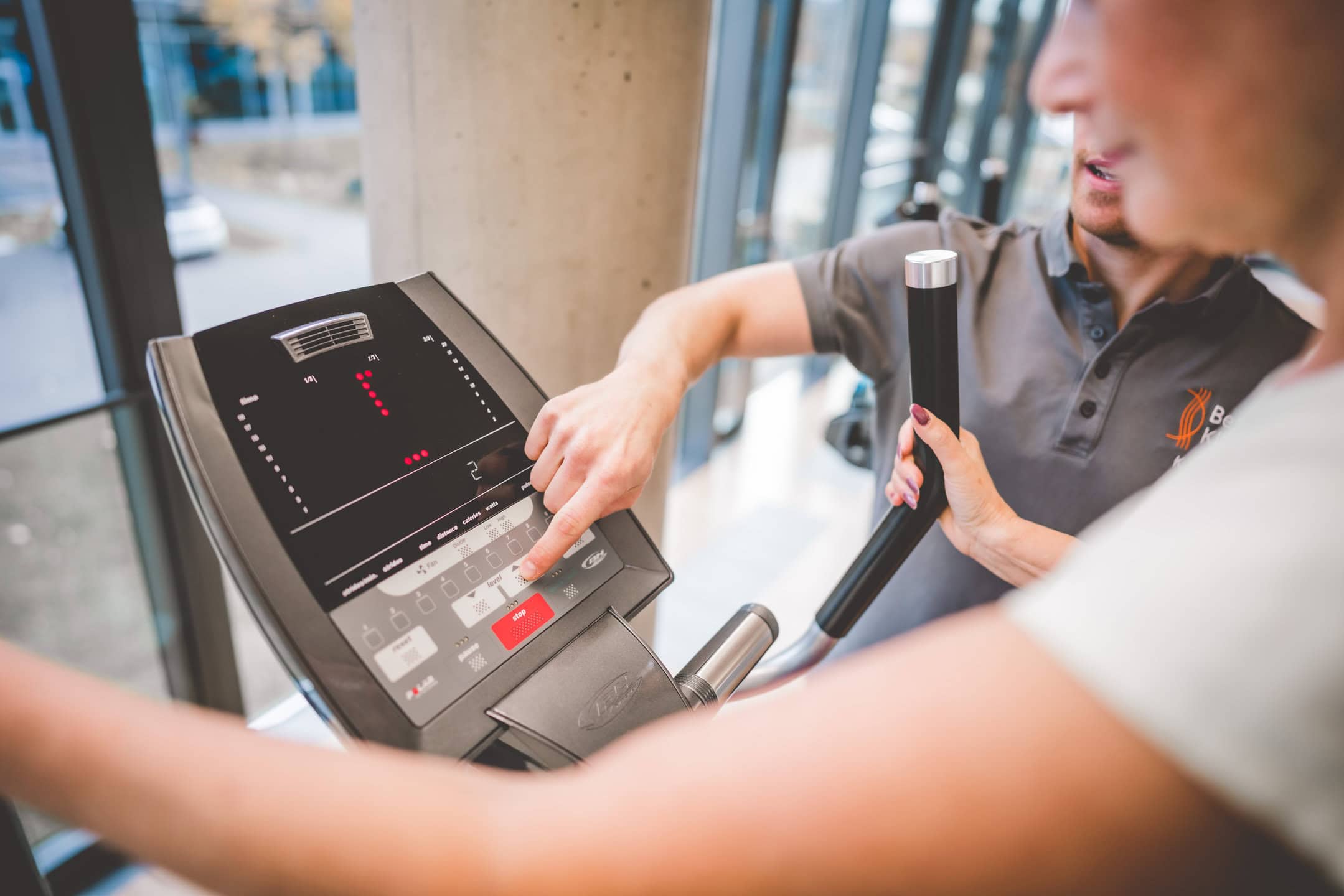 Zwei Personen bedienen zusammen ein Laufband in einem hellen Fitnessstudio.