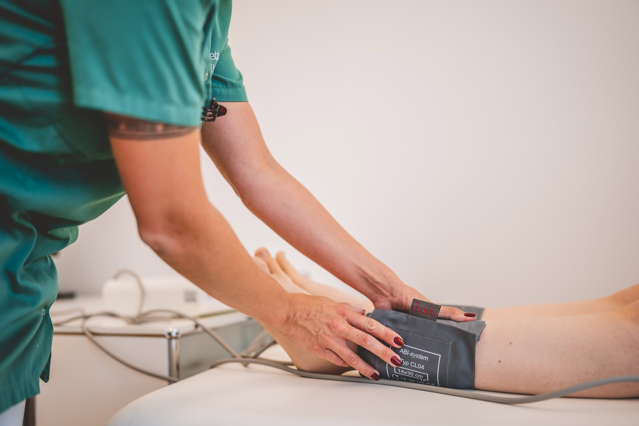 Medizinisches Personal in grüner Uniform legt Blutdruckmanschette an Bein an.
