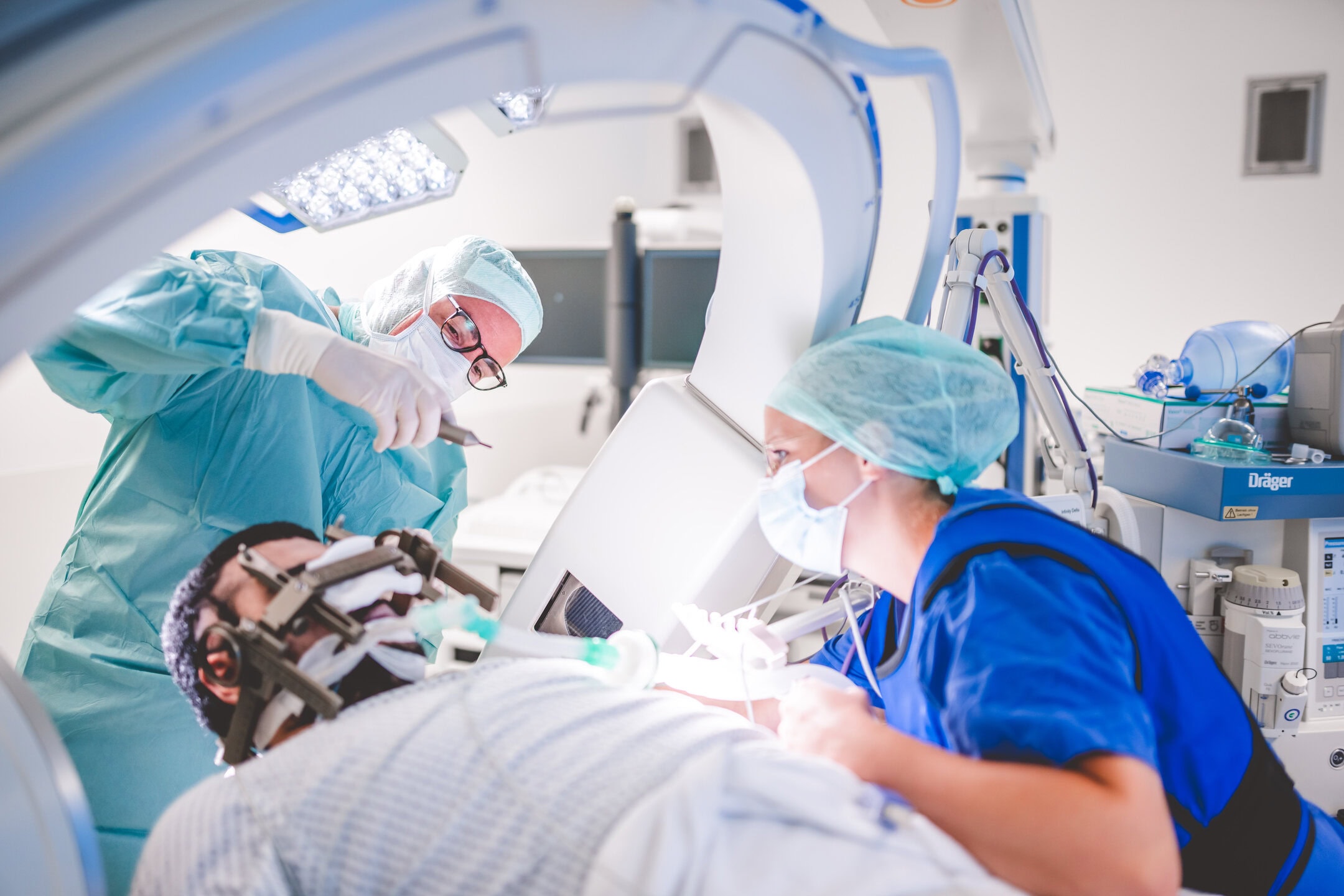 Chirurgen in OP-Kleidung operieren einen Patienten mit Kopfhalterung unter einem großen medizinischen Gerät.
