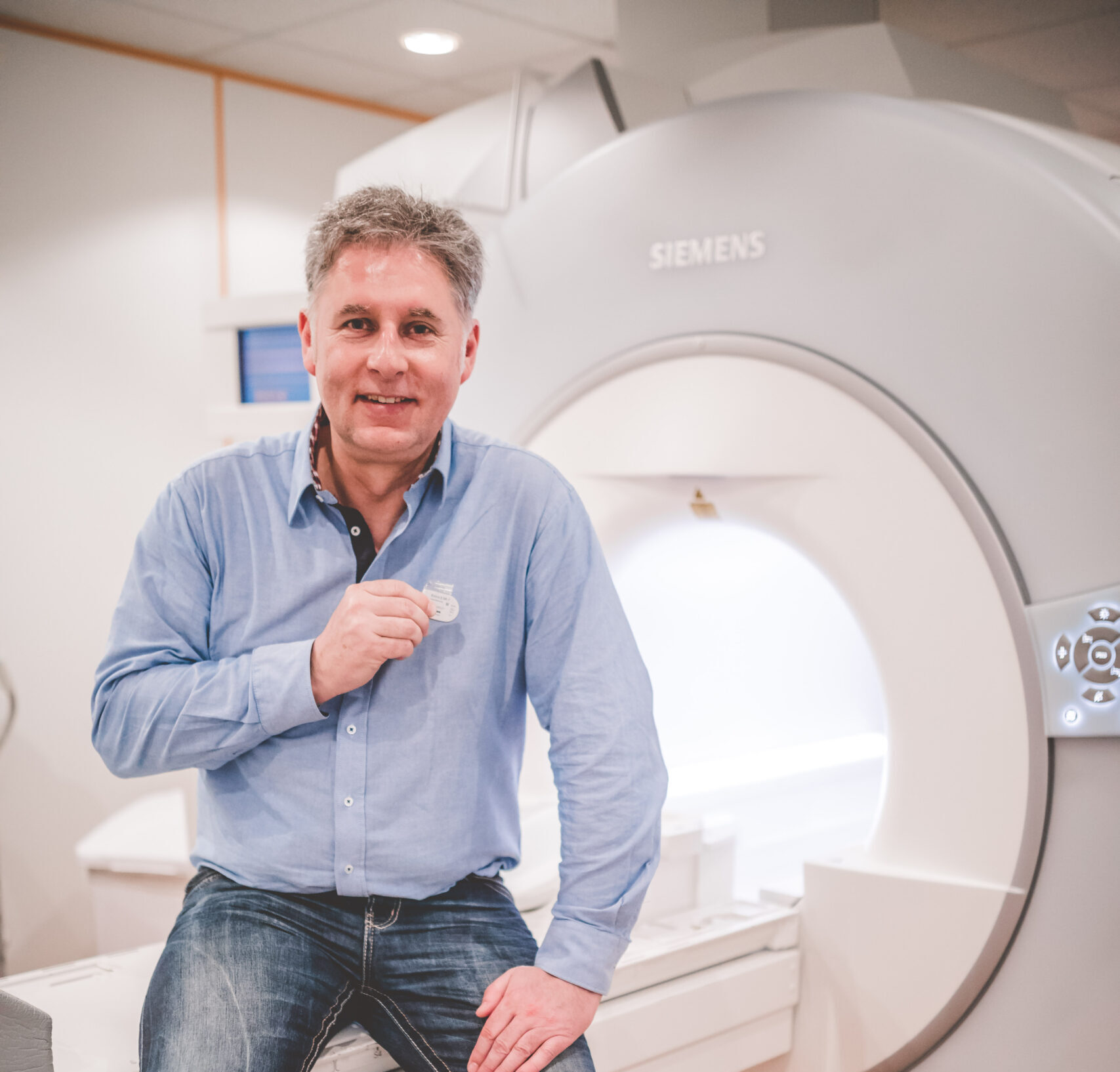 Ein Mann im blauen Hemd sitzt vor einem großen, grauen MRT-Gerät.