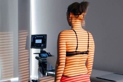 Eine Frau in Sportkleidung steht in einem Raum, Sonnenlicht wirft Streifenmuster auf ihren Rücken.