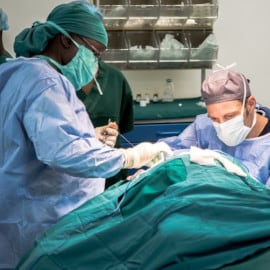 Chirurgen in blauer OP-Kleidung führen eine Operation in einem sterilen OP-Saal durch.