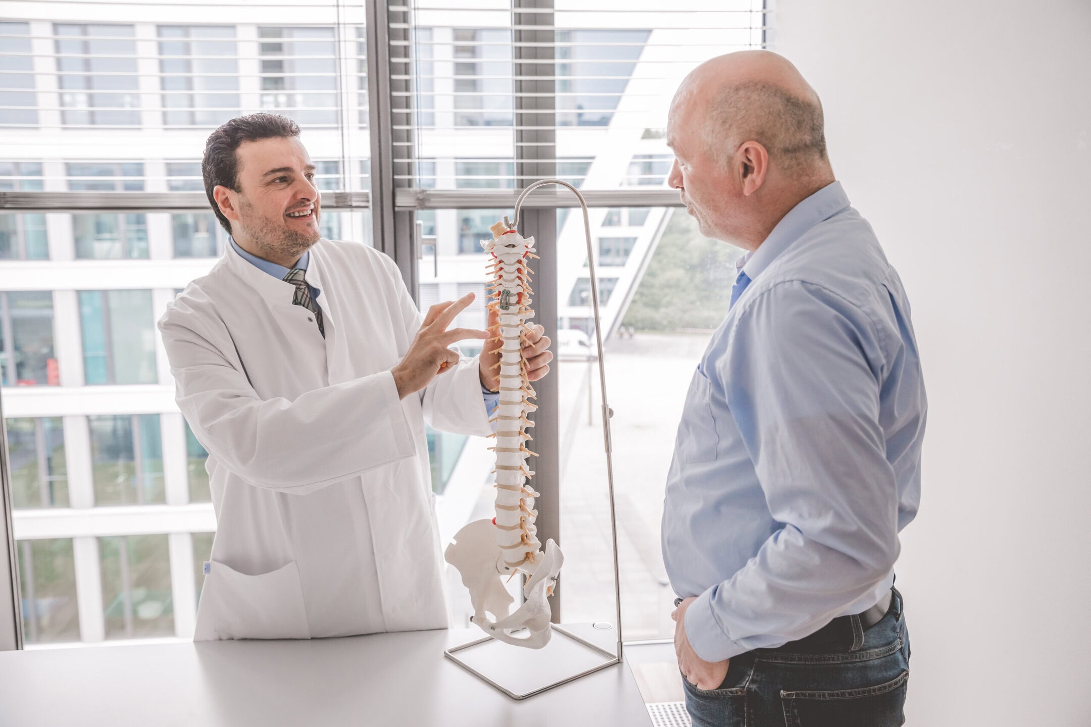 Ein Arzt erklärt einem Mann ein Wirbelsäulenmodell in einem modernen Büro.