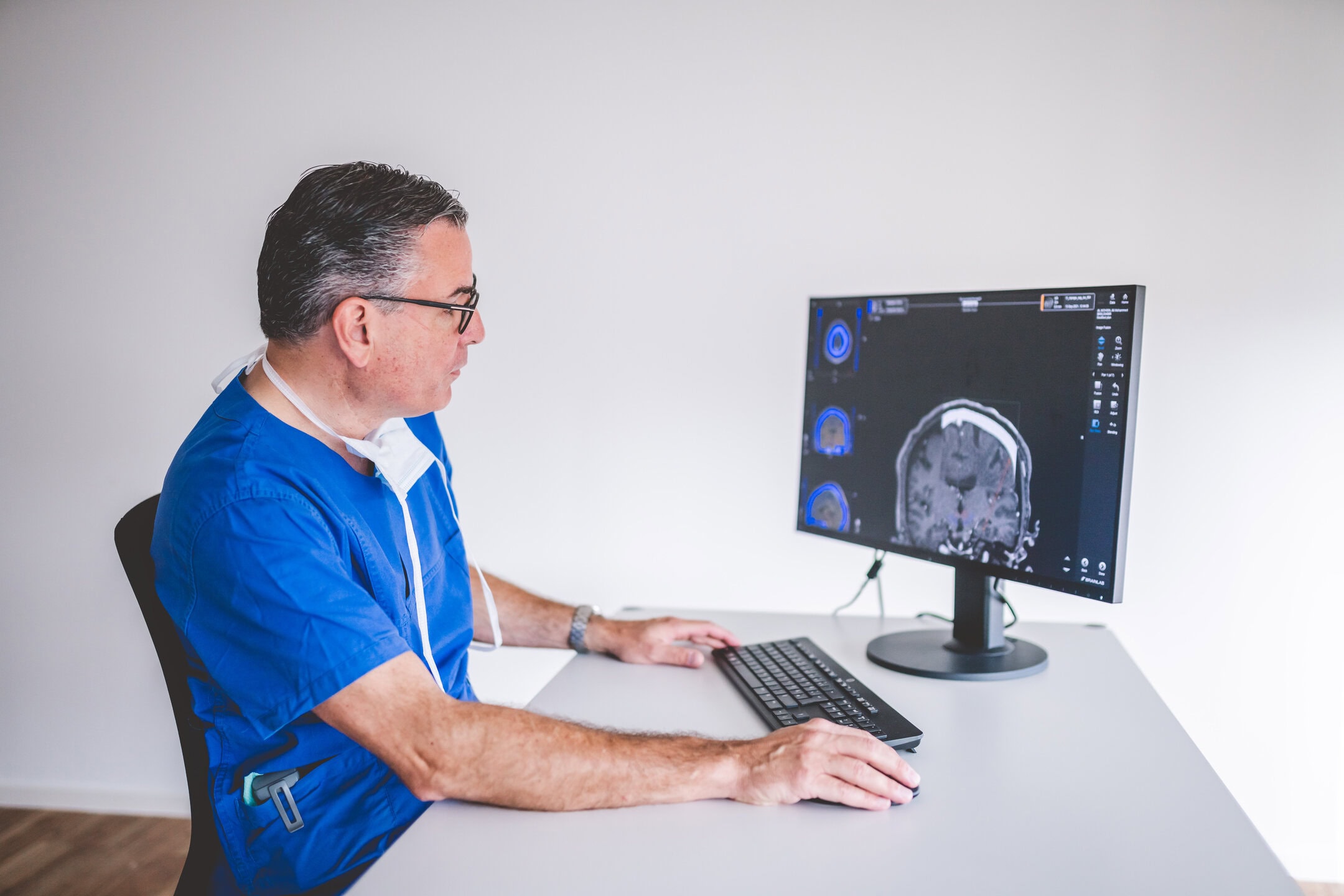 Ein Arzt in blauer Kleidung betrachtet ein MRT-Bild auf einem Computermonitor.