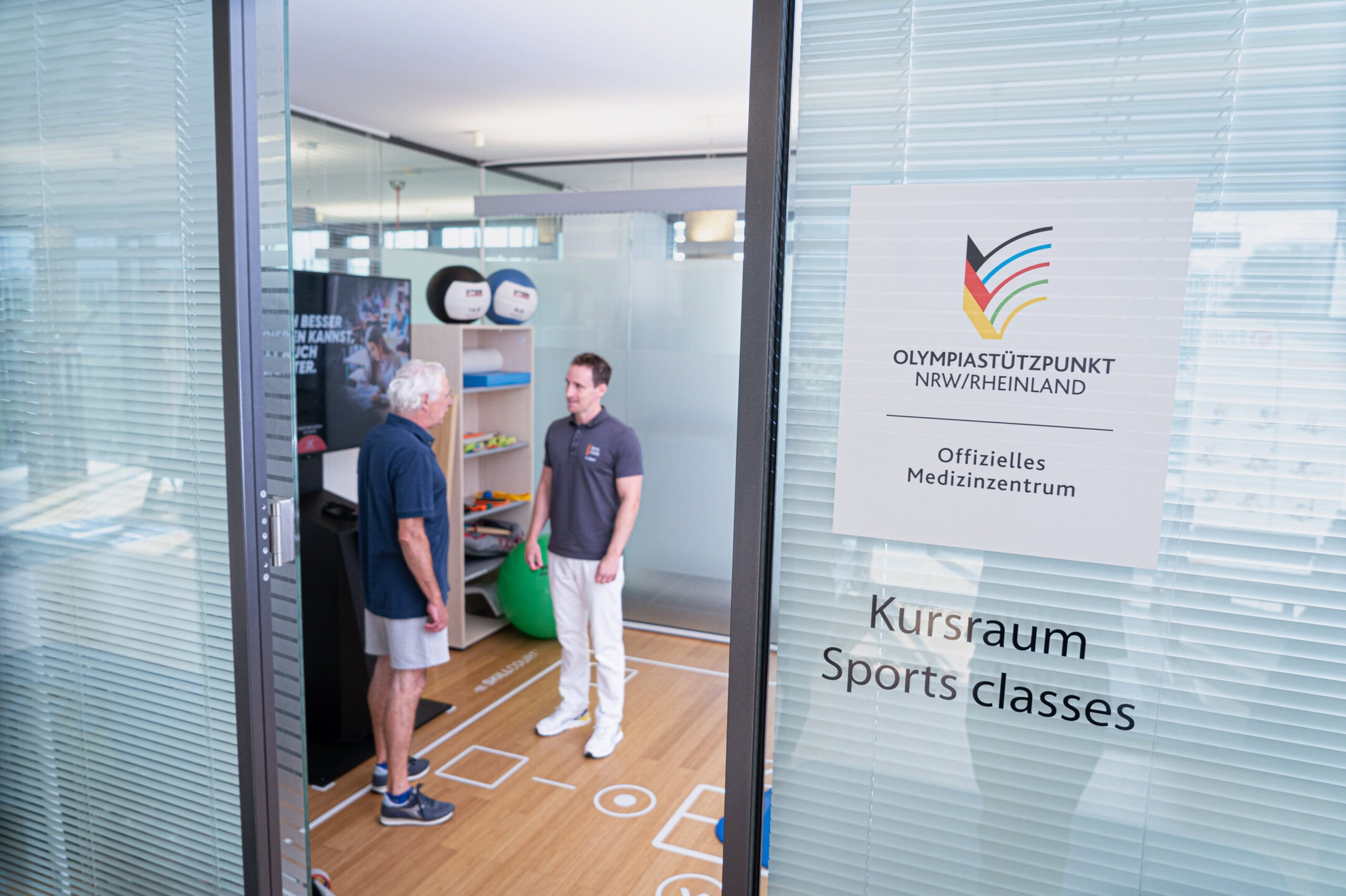 Physiotherapeut steht mit Patienten im Kursraum