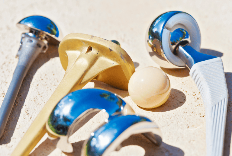 Verschiedene Hüftprothesenteile aus Metall und Keramik liegen auf einer cremefarbenen Oberfläche.